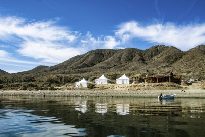 White luxury safari-style glamping tents on the desert shore, viewed from the waters of Magdalena Bay, Baja California Sur."
